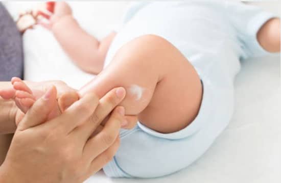 mother rubbing in baby healing cream to her baby's lower leg using her fingers